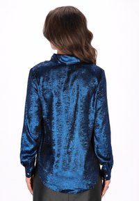 Hosszú ujjú ing csillogó tengerészkék szövetből, galléros nyakkivágással, gombos mandzsettákkal és enyhén ívelt szegéllyel, texturált felülettel.