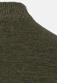 Strickpullover in tiefgrün mit geripptem Textur, ausgestattet mit einem hohen Kragen. Der Stoff hat ein dezent gewebtes Muster mit leichten Farbvariationen.