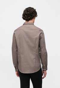 Braunes Langarmhemd aus strukturiertem Stoff mit geknöpften Manschetten und klassischem Kragen. Rückansicht zeigt einen geraden Saum und Nähte.