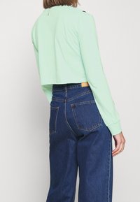 Mintgrön kortärmad tröja med rund halsringning, matchad med högmidjade blå denimjeans som har bakfickor och bältesloopar.