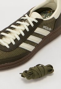 Gröna och krämfärgade Adidas Spezial-sneakers med texturert ovandel, vita snören och brun gummisula; inkluderar en extra grön skosnöre.