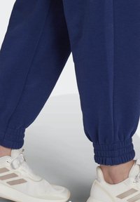 Navyblauwe joggers met Gathered enkels, gemaakt van zachte stof, gecombineerd met witte sportschoenen met neutrale accenten.