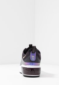 Nike sneaker features a black upper with mesh texture, purple gradient heel, and a patterned sole. Gold accent on lateral side.