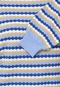 Pull en tricot avec un motif répétitif de diamants en bleu, beige et blanc, avec un poignet côtelé bleu clair. Texture douce, coupe ajustée.