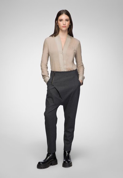 Sheer beige button-up blouse with a V-neck, paired with dark gray tailored trousers featuring a diagonal front seam and zipper accent. Black platform boots.