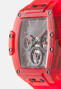 Montre rouge transparente avec un boîtier rectangulaire, un cadran noir, des éléments en acier inoxydable et des détails d'accent. Comprend trois sous-cadrans et de grands index horaires.