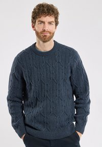 Ciemnoniebieski sweter z dzianiny, z teksturowanym wzorem w warkocz, okrągłym dekoltem oraz ściągaczami przy mankietach i na dole. Miękki materiał, luźny krój.