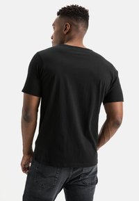 Sort kortærmet T-shirt med rund hals, lavet af bomuld, med en glat tekstur og en klassisk pasform, båret med mørke jeans.