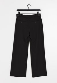 Svarta vida byxor med en mjuk textur, med bakfickor och en platt midja, hängande på en svart galge mot en vit bakgrund.