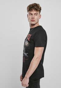 Czarny bawełniany t-shirt z grafiką Tupaca na przodzie, z czerwonymi i szarymi elementami tekstowymi, krótkimi rękawami i okrągłym dekoltem.