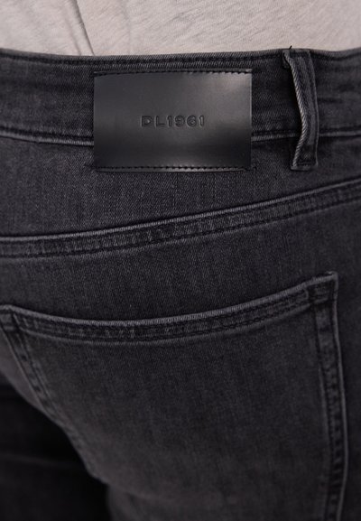 Jean en denim gris foncé avec une étiquette en cuir portant l'inscription "DL1961" sur la taille, avec des surpiqûres contrastantes et des poches arrières classiques.