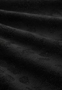 Close-up van zwart stof met verhoogde, getextureerde stippen die een subtiel patroon vormen op een zachte, licht gerimpelde ondergrond.