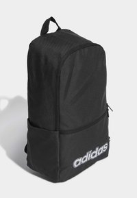 Zaino nero realizzato in tessuto resistente, con forma rettangolare, una tasca frontale con zip e un grande logo bianco sul lato.