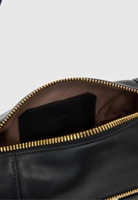 Zwarte leren tas interieur met een gladde textuur, gouden rits en bruine voering. Inclusief een klein zwart label.