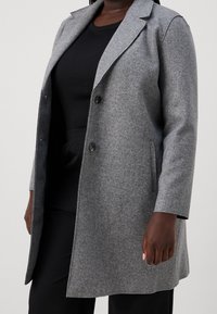 Szary płaszcz z wełny z wyciętym kołnierzem, dwiema guzikami, kieszeniami bocznymi i długimi rękawami; teksturowana powierzchnia z gładkim wykończeniem.