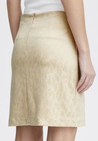 Jupe beige avec un imprimé animal subtil, dotée d'une coupe ajustée, d'un tissu texturé et d'une fermeture éclair au dos.