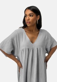 Lichtgrijze jurk van gestructureerde stof, met een V-hals, losse mouwen en een geplooide taille voor een comfortabele pasvorm.