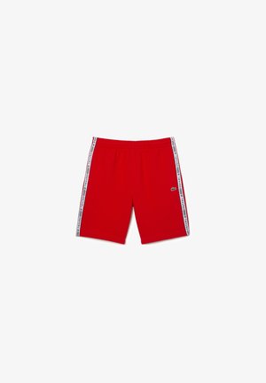 Pantalones cortos deportivos rojos con rayas laterales blancas que presentan texto con el logo y un pequeño logo de cocodrilo en el muslo izquierdo.