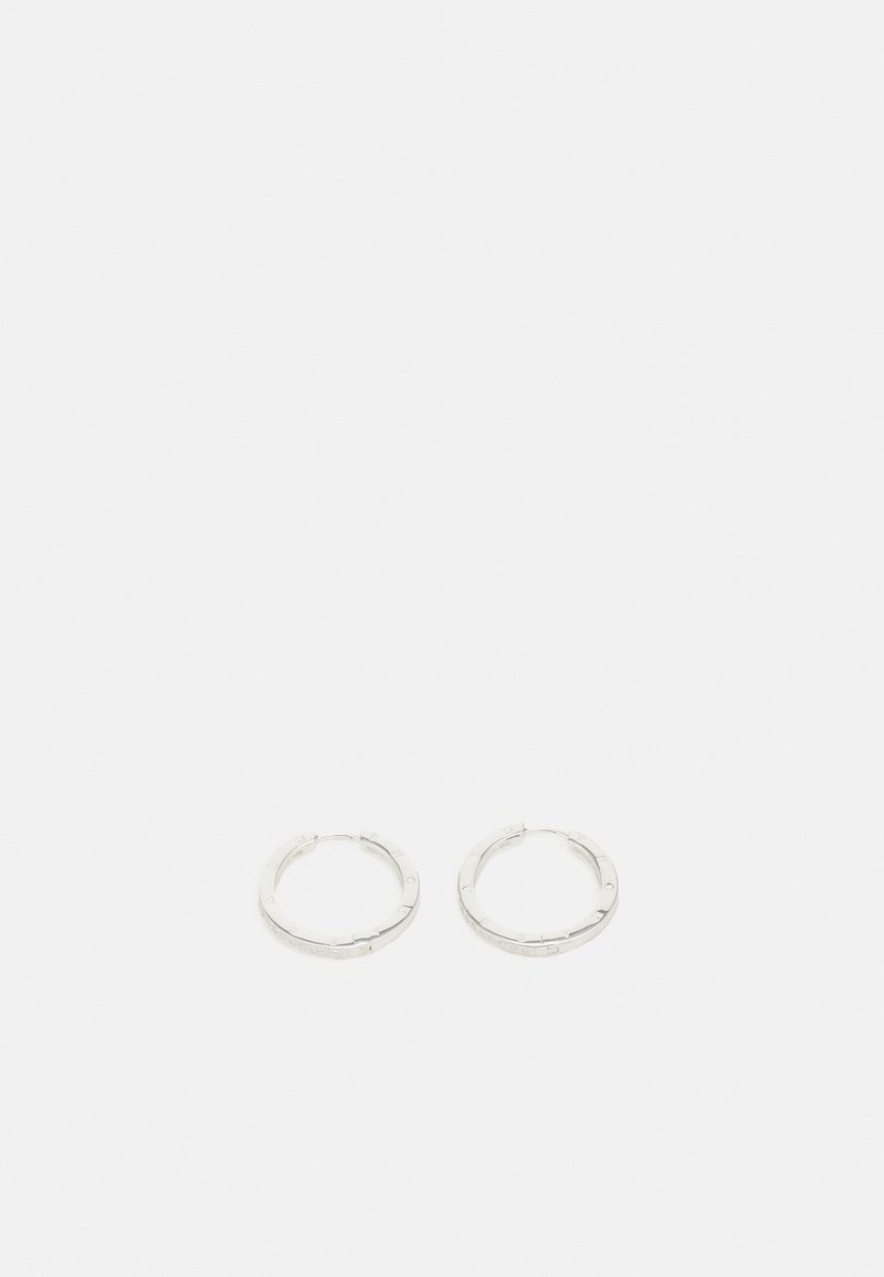 Par de pendientes de aro de plata con sutiles detalles grabados, colocados sobre un fondo blanco liso.