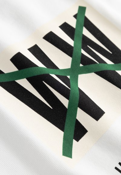 Hvitt stoff med en strukturert overflate som har et svart og grønt grafisk design. Svarte linjer krysser en diagonal grønn stripe.