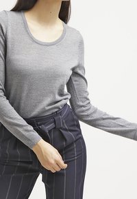 Harmaa pitkähihainen neulepaita, jossa pyöreä pääntie. Yhdistetty laivastonsinisiin, raidallisiin housuihin, joissa on vyö.