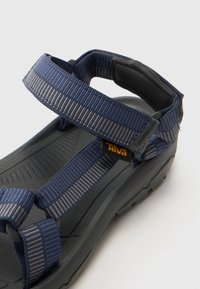 Mørkeblå sandal med teksturert svart såle, som har justerbare nylonstropper og en polstret såle. Teva-logo på stroppen.