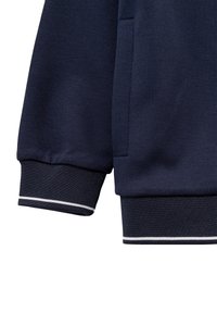 Polsino di felpa blu navy con texture a coste e accentuazione a striscia bianca. Materiale morbido in cotone misto; vestibilità standard con cuciture visibili.