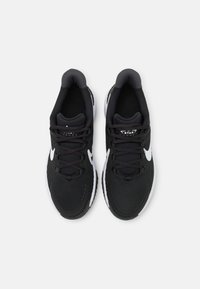 Zapatillas deportivas negras con parte superior de tela texturizada, puntera reforzada, logo blanco en forma de swoosh y cordones planos. Suela de goma con un patrón de banda distintivo.