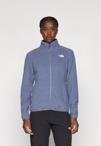 Fleece striukė švelniai mėlynos spalvos su aukštu apykaklės, visiškai užtraukiama ir dviem šoninėmis kišenėmis. Ant kairiojo krūtinės ploto yra baltas logotipas.