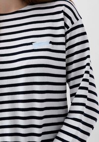 Long-sleeve striped sweater featuring black and white horizontal stripes and a light blue logo patch on the left chest. Soft knit fabric.