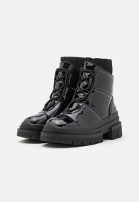 Bottines en cuir verni noir avec une semelle en caoutchouc épaisse, un design rehaussé, un laçage sur le devant, un col en tricot à la cheville et une finition texturée.