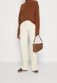 Bruine geribde trui, crème wijde broek, bruine leren tas met gouden hardware en donkere schoenen met lichte zolen.