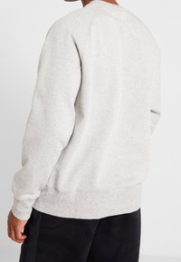 Sudadera gris claro con textura salpicada, puños y dobladillo acanalados. Presenta un cuello redondo y mangas raglán. Ajuste informal.
