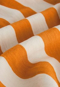 Orange-weiß gestreifter Stoff mit sichtbarer Textur, in Nahaufnahme mit weichen Falten und sanfter Beleuchtung gezeigt.