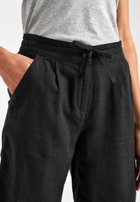 Zwarte linnen broek met een taille met trekkoord, zijzakken en een comfortabele pasvorm. De stof heeft een zachte, gestructureerde afwerking.