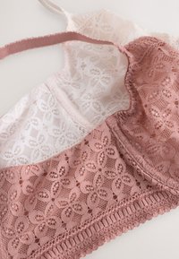 Bralette in pizzo rosa cipria e bianco con motivi floreali, spallina regolabile e bordo smerlato, disteso su uno sfondo bianco.