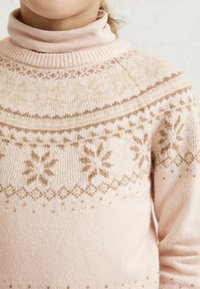 Osoba oblečená v svetlom ružovom pletenom svetri s béžovými vzormi snežienok a so svetloružovým rolákom pod ním.