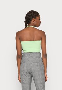 Top cropped halter em verde menta ribeteado, combinado com calças de cintura alta xadrez cinzentas. O top tem uma silhueta ajustada e uma textura suave.