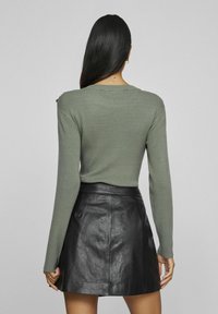 Geribbeld groen lang mouwen top met een ronde halslijn, gecombineerd met een zwarte leren rok. De rok heeft een gladde, glanzende textuur.