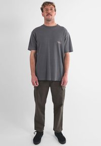 T-shirt gris en coton avec un petit logo brodé sur la poitrine gauche, associée à un pantalon cargo olive avec poches latérales et des baskets noires.