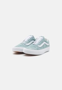 Des baskets en suède bleu clair présentant un design à rayures blanches, des lacets blancs et une semelle en caoutchouc blanche. Surface texturée et bout arrondi.
