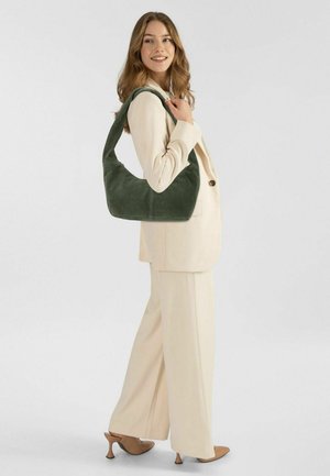 Borsa a spalla verde in suede con una forma curvilinea e un'ampia tracolla, abbinata a un completo crema. Texture liscia e dettagli hardware minimali.