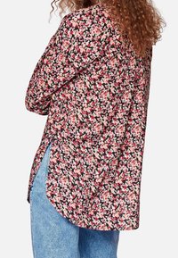 Camicia nera floreale con fiori rosa e bianchi, maniche lunghe, fessure laterali e orlo arrotondato. Realizzata in tessuto leggero, adatta per essere indossata a strati.