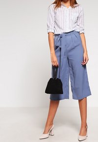 Ljusblå culotte-byxor med knyt i midjan, ihop med en vit och randig skjorta med knappar, samt en svart handväska. Beige klackskor med blockhäll.