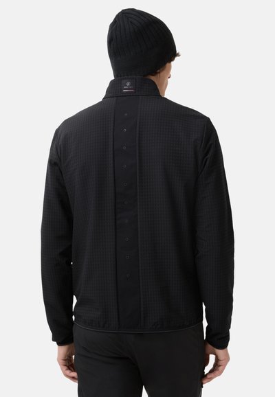 Schwarze Jacke mit strukturiertem Muster, Druckknopfverschluss auf der Rückseite und einem Kragen Design. Kombiniert mit einer gestrickten schwarzen Mütze.
