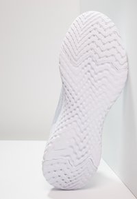 Semelle de baskets blanches affichant un motif en zigzag avec de petites indentations rondes ; texturée pour l'adhérence, elle présente une légère courbure.