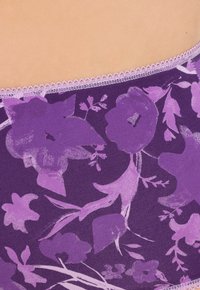 Tissu à motif floral violet avec différentes nuances de violet, présentant un délicat bord en dentelle lilas clair le long de la taille.