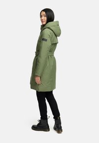 Grøn polstret parka med bælte, hætte og lynlåslommer. Designet med en glat tekstur og et logo-patch på ærmet. Sorte bukser og støvler.