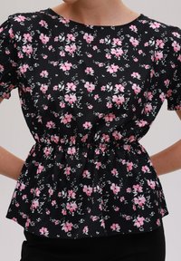 Svart blommigt linne med rosa blommor, kort puffärmar, resår i midjan, lättviktsmaterial och rund halsringning.