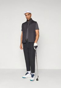 Juodas be rankovių liemenė dėvima ant pilkos polo marškinėlių, juodos kelnės, baltos spalvos batai su mėlynais akcentais. Laiko golfo lazdelę, dėvi baltą kepurę ir golfo pirštinę.